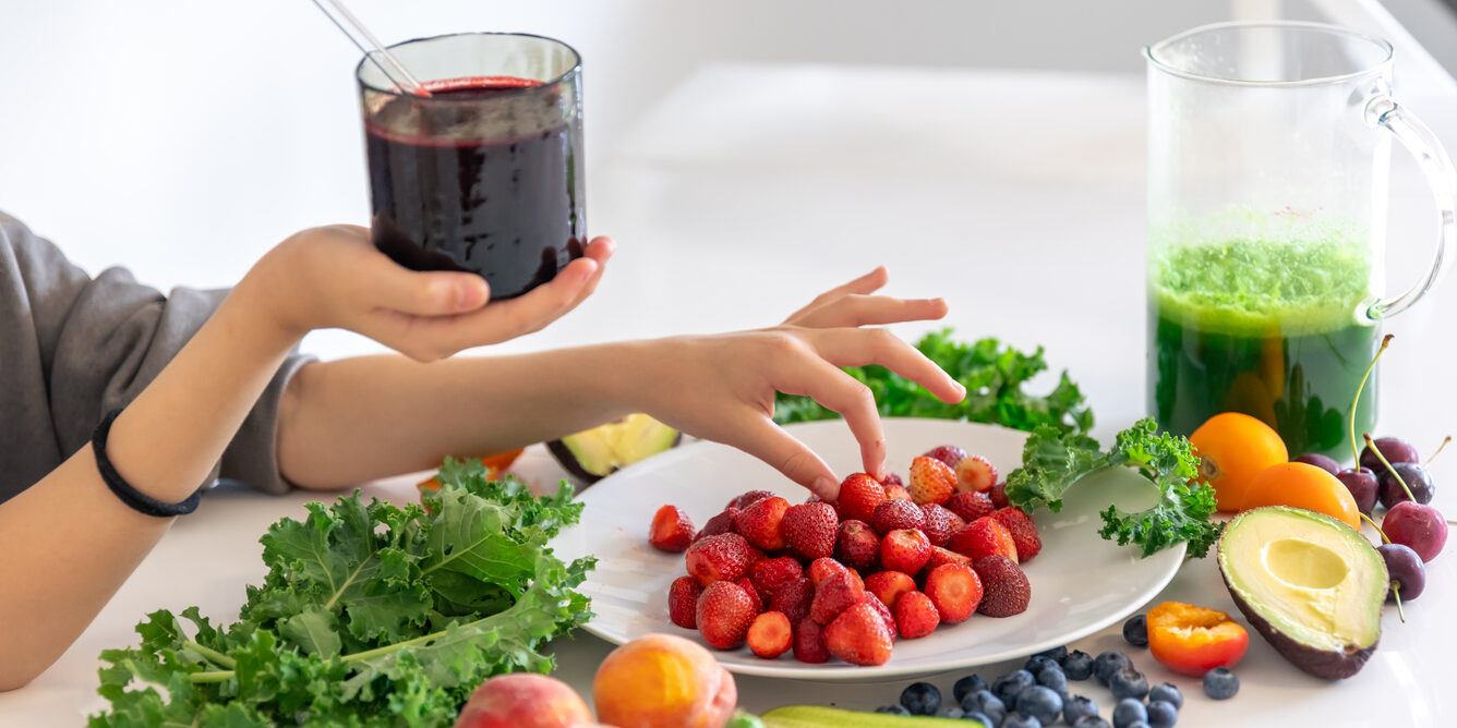 A glass of smoothie from berries in a child’s hand at home in the kitchen.