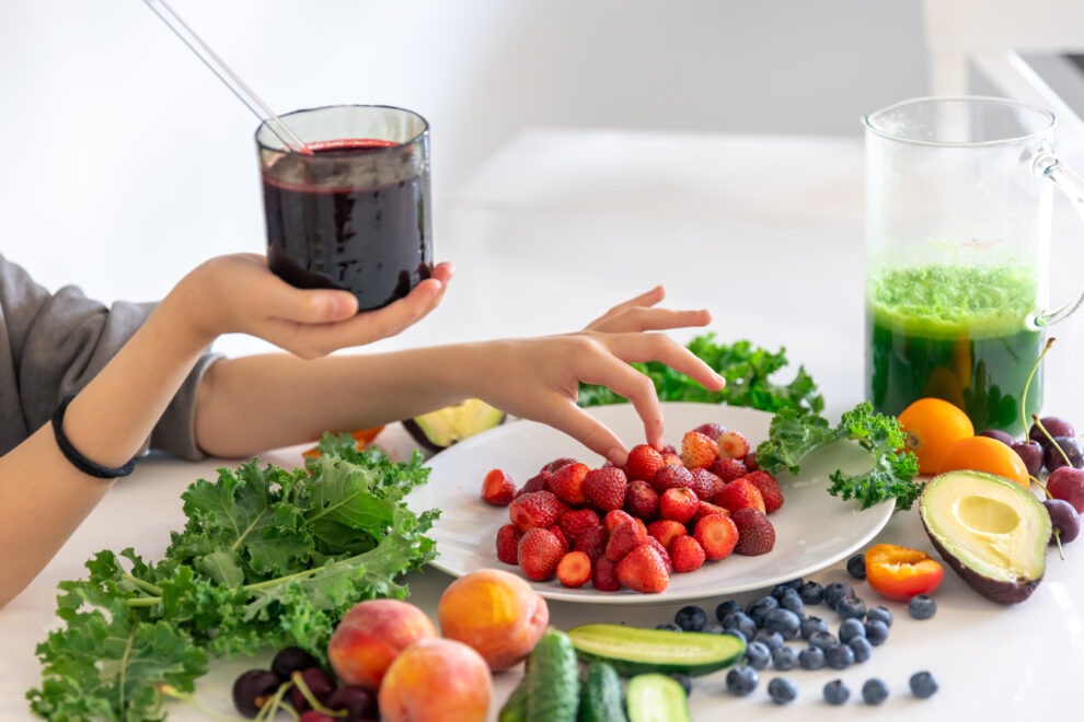 A glass of smoothie from berries in a child’s hand at home in the kitchen.