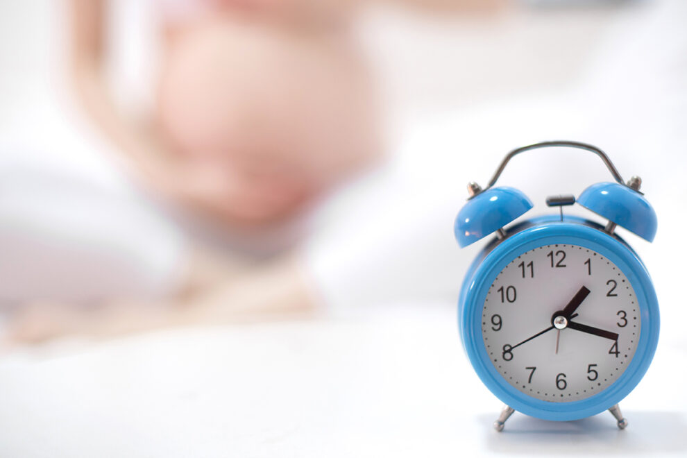 Closeup photo of pregnant woman holding red alarm clock at tummy